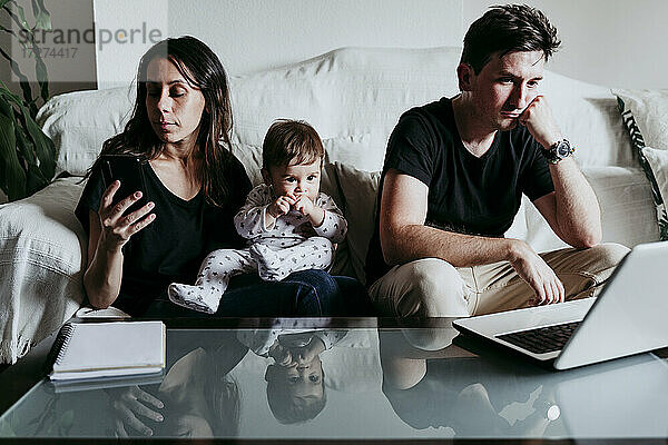 Die Mutter benutzt ein Smartphone  während der Vater am Laptop arbeitet und der Sohn zu Hause sitzt