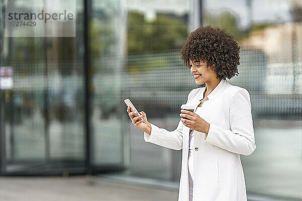 Geschäftsfrau mit Kaffeetasse  die im Freien stehend ein Mobiltelefon benutzt