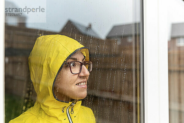 Frau schaut durch das Fenster  während sie zu Hause in der Regenzeit steht