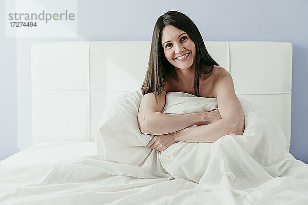 Lächelnde schöne Frau sitzt auf dem Bett zu Hause
