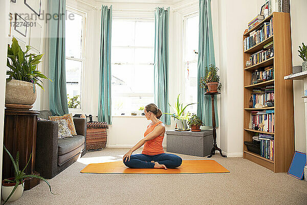 Ältere Frau macht Yoga-Übungen auf einer Matte sitzend zu Hause