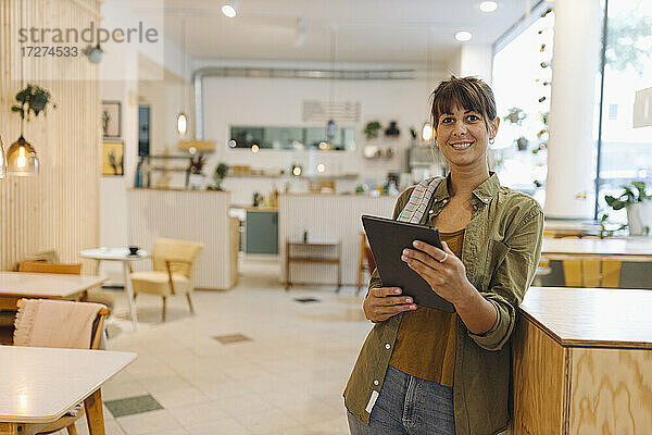 Lächelnde Besitzerin mit digitalem Tablet in einem Café stehend