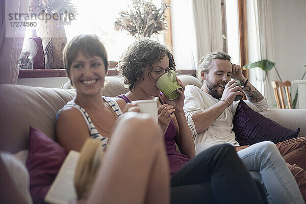Männliche und weibliche Freunde trinken Kaffee  während sie zu Hause auf dem Sofa sitzen