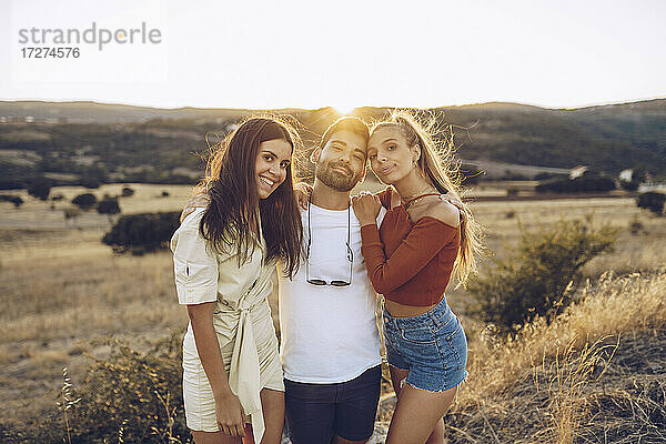 Lächelnder junger Mann mit Freundinnen auf einem Feld stehend