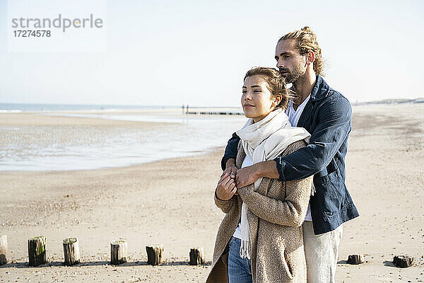 Junges Paar schaut weg und umarmt sich am Strand