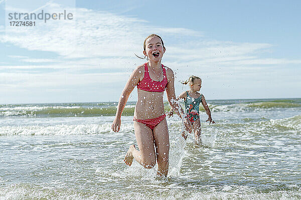 Mädchen laufen im Wasser am Strand an einem sonnigen Tag