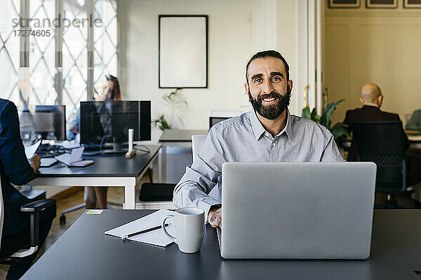 Selbstbewusster Hipster-Unternehmer bei der Arbeit am Laptop am Schreibtisch im Büro