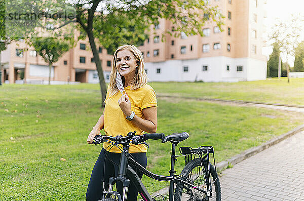 Lächelnde Frau mit Fahrrad auf dem Fußweg in der Stadt während COVID-19