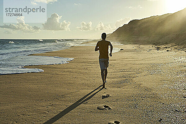Mann joggt bei Sonnenuntergang auf Sand am Strand