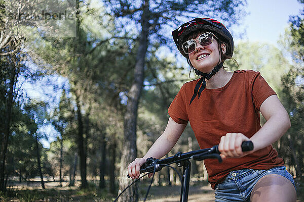 Glückliche junge Frau auf dem Fahrrad gegen Bäume auf dem Lande