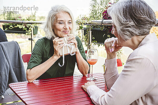 Glückliche Frau mit Geschenk in der Hand  während sie mit einer Freundin im Restaurant sitzt