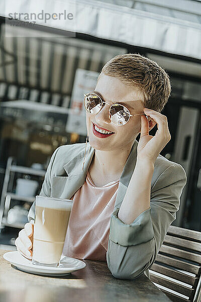 Mittlere erwachsene Frau mit Sonnenbrille und Kaffeeglas in einem Straßencafé an einem sonnigen Tag
