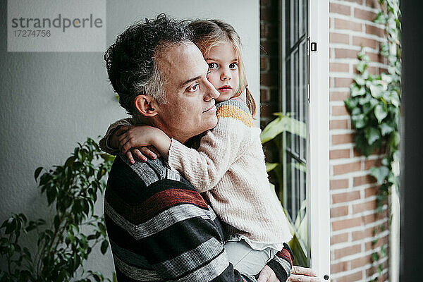 Vater mit Tochter schaut durch das Fenster  während er zu Hause steht