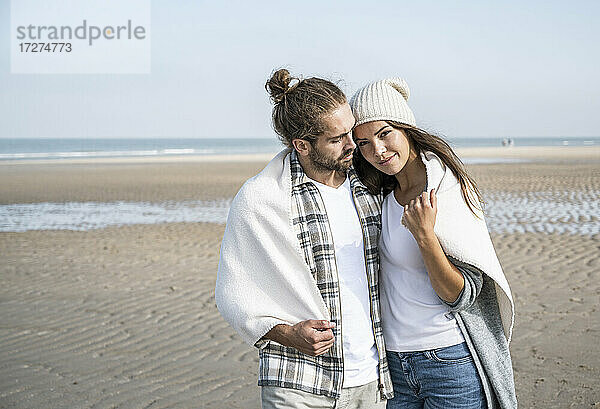 Junges  in eine Decke gehülltes Paar  das am Wochenende seine Freizeit am Strand verbringt