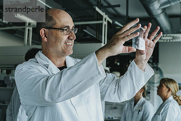 Wissenschaftlerin lächelt bei der Untersuchung eines Objektträgers mit menschlichem Gehirn  während ein Mitarbeiter im Hintergrund im Labor steht