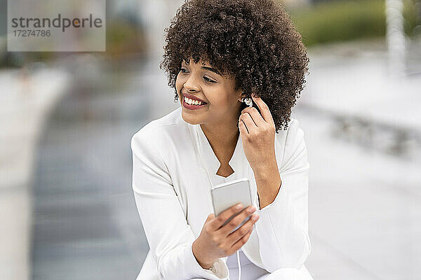 Lächelnde Geschäftsfrau  die wegschaut  während sie im Freien ein Mobiltelefon benutzt