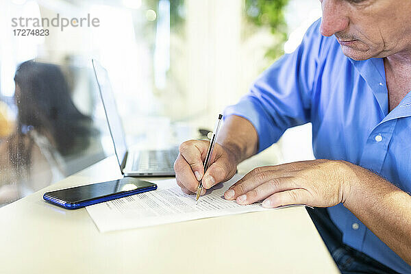 Reifer männlicher Unternehmer  der in einem Café sitzt und auf einem Papier schreibt
