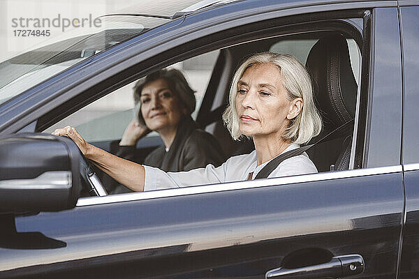 Geschäftsfrau sitzt mit einem Kollegen am Steuer eines Autos in der Stadt