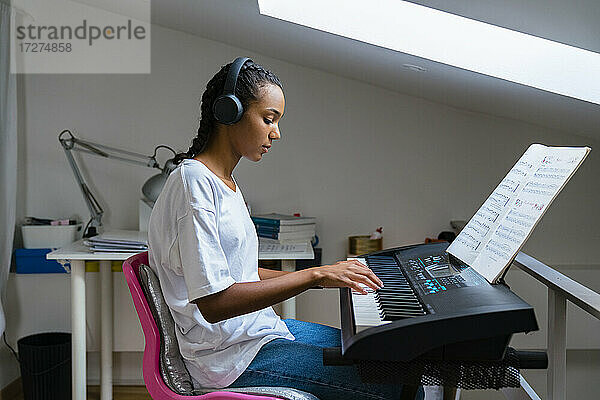 Teenager-Mädchen spielt Klavier  während sie zu Hause sitzt