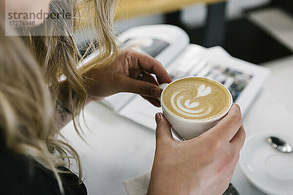 Frau hält Cappuccino-Tasse  während sie in einem Café sitzt