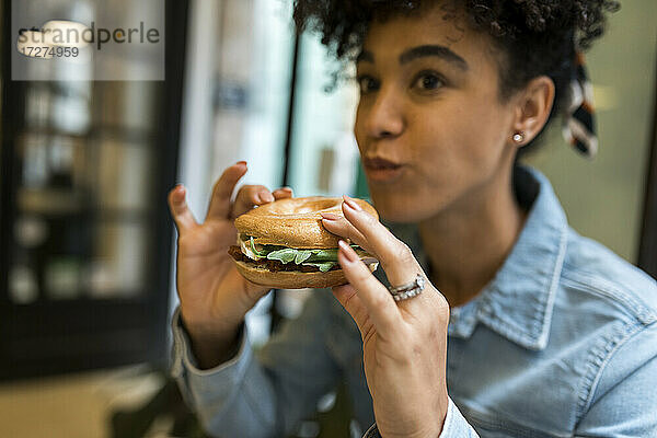Mittlere erwachsene Frau  die im Café sitzend einen Burger isst