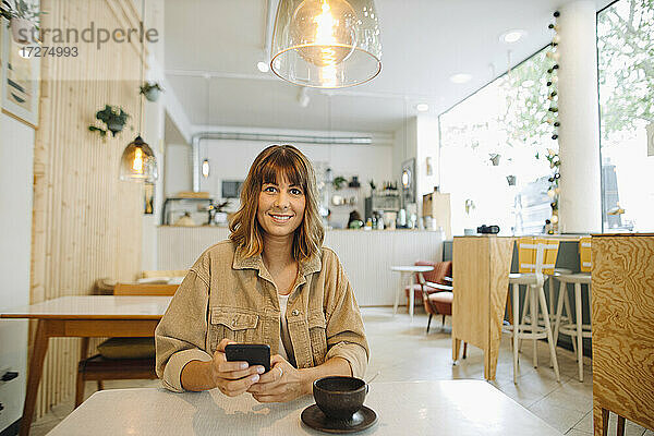 Geschäftsfrau  die in einem Café sitzt und ihr Smartphone benutzt