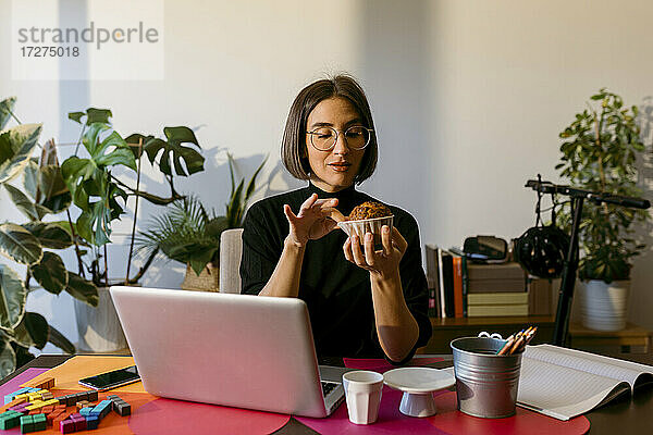 Mid adult businesswoman holding cake while sitting by laptop at home