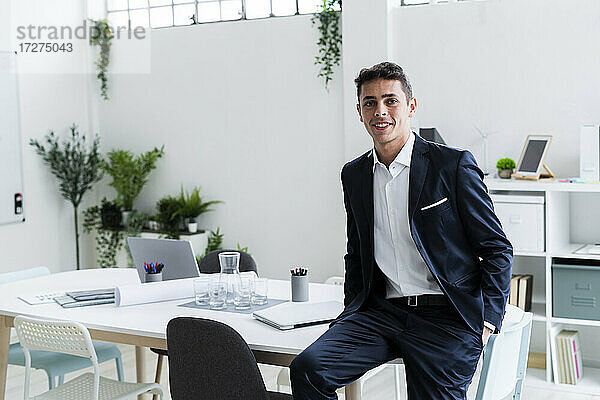 Lächelnder männlicher Unternehmer am Schreibtisch sitzend an einem kreativen Arbeitsplatz