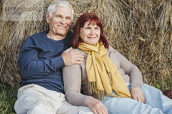 Glückliches älteres Paar  das sich auf einem Feld an einen Heuballen lehnt