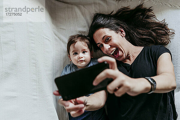 Mutter und Sohn machen ein Selfie mit dem Smartphone  während sie zu Hause im Schlafzimmer liegen