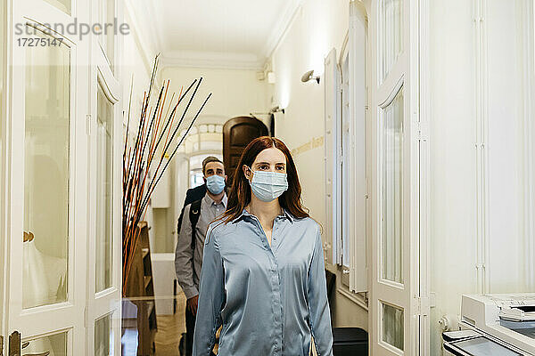 Geschäftsfrau mit Gesichtsschutzmaske geht mit Kollegen im Korridor spazieren