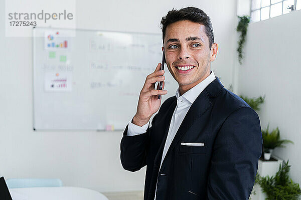 Glücklicher männlicher Berufstätiger  der beim Telefonieren am Arbeitsplatz wegschaut