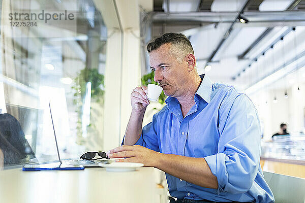Männlicher Unternehmer trinkt Kaffee und schaut in einem Café auf seinen Laptop