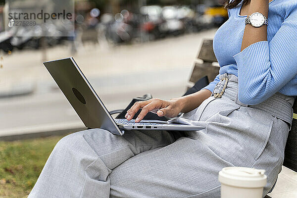 Frau surft im Internet auf einem Laptop  während sie auf einer Bank sitzt