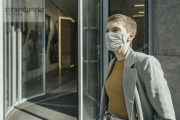 Mittlere erwachsene Frau mit Gesichtsschutzmaske vor einem Eingang stehend