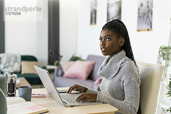 Junge Frau  die wegschaut  während sie zu Hause am Laptop sitzt und studiert