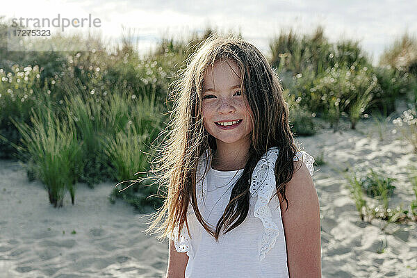 Lächelndes Mädchen  das an einem sonnigen Tag am Strand im Sand steht