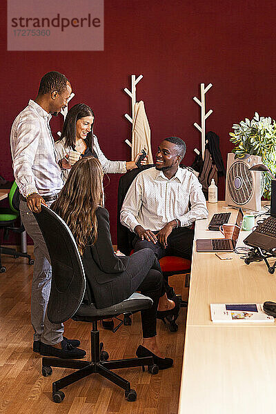 Lächelnde multiethnische männliche und weibliche Kollegen diskutieren bei einer Besprechung im Büro