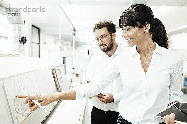 Lächelnde Technikerin  die auf eine Grafik zeigt  während sie mit einem männlichen Kollegen im Labor diskutiert