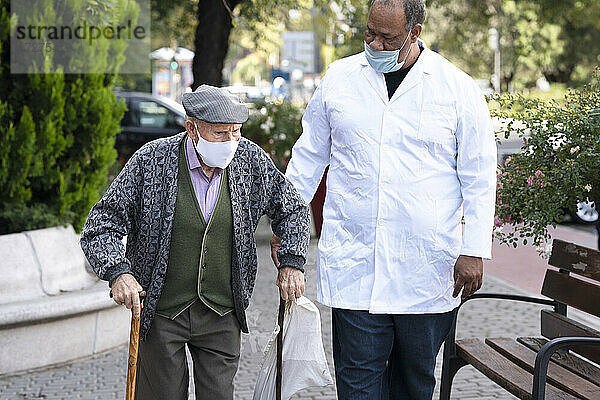 Reifer Mann mit älterem Mann mit Gesichtsschutzmaske beim Spaziergang im Freien
