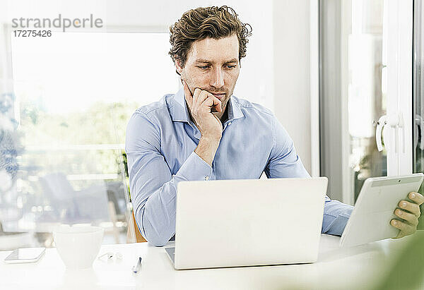 Mittelgroßer erwachsener Mann  der im Büro sitzend ein digitales Tablet benutzt