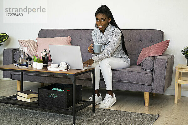Junge Geschäftsfrau trinkt Kaffee  während sie zu Hause am Laptop arbeitet