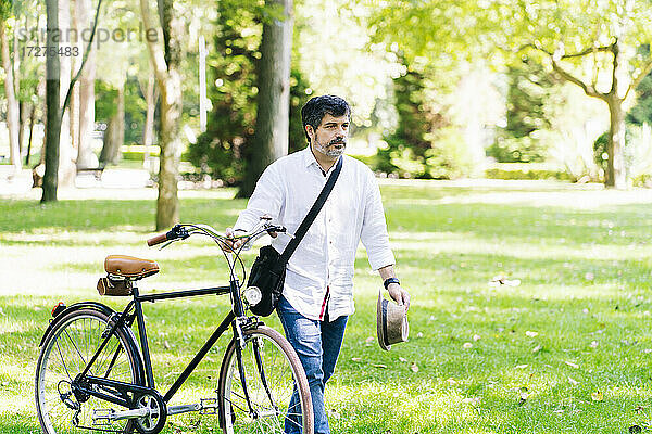 Älterer Mann mit Fahrrad auf Gras in einem öffentlichen Park