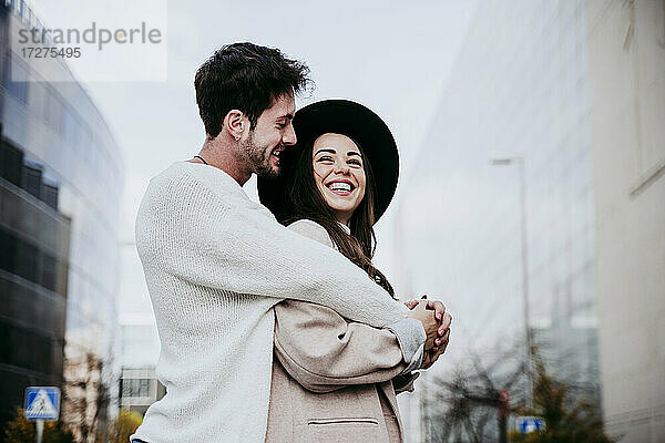 Lächelnder Mann umarmt  während er seine Partnerin gegen den Himmel in der Stadt betrachtet
