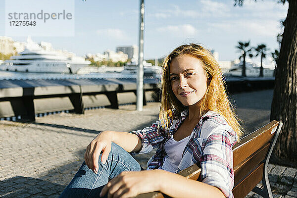 Junge Frau sitzt auf einer Bank an einem sonnigen Tag