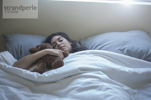 Junge Frau hält Spielzeug  während sie auf dem Bett zu Hause schläft