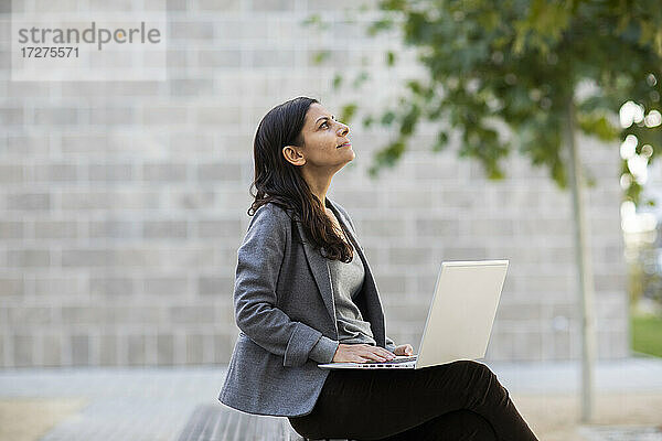 Geschäftsfrau  die einen Laptop benutzt und auf einer Bank an der Wand sitzt