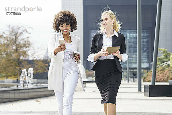 Lächelnde Geschäftsfrauen mit Smartphone und digitalem Tablet auf dem Gehweg