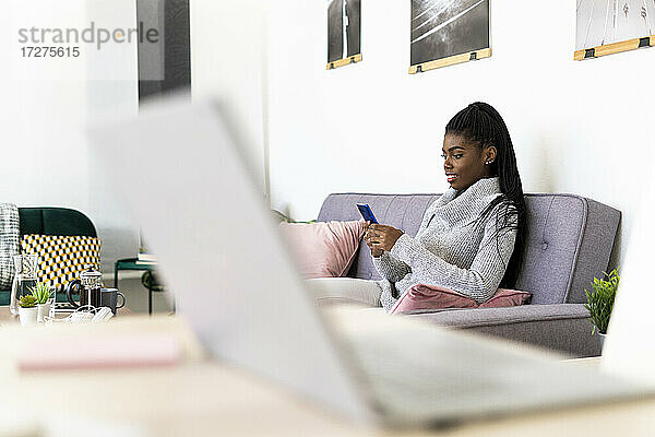 Frau benutzt Smartphone  während sie zu Hause auf dem Sofa sitzt