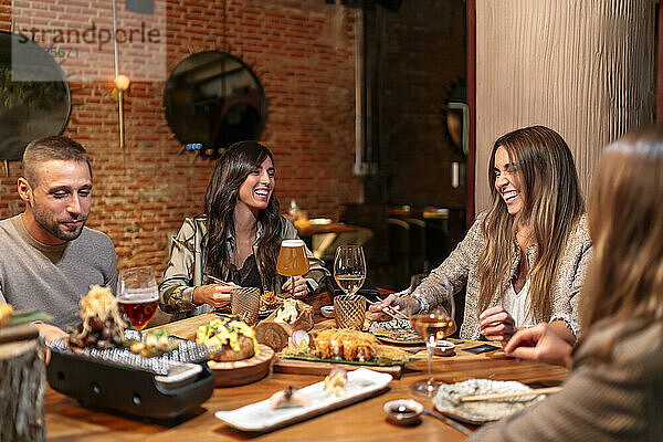 Lächelnde Freunde  die Essen und Trinken genießen  während sie am Tisch im Restaurant sitzen